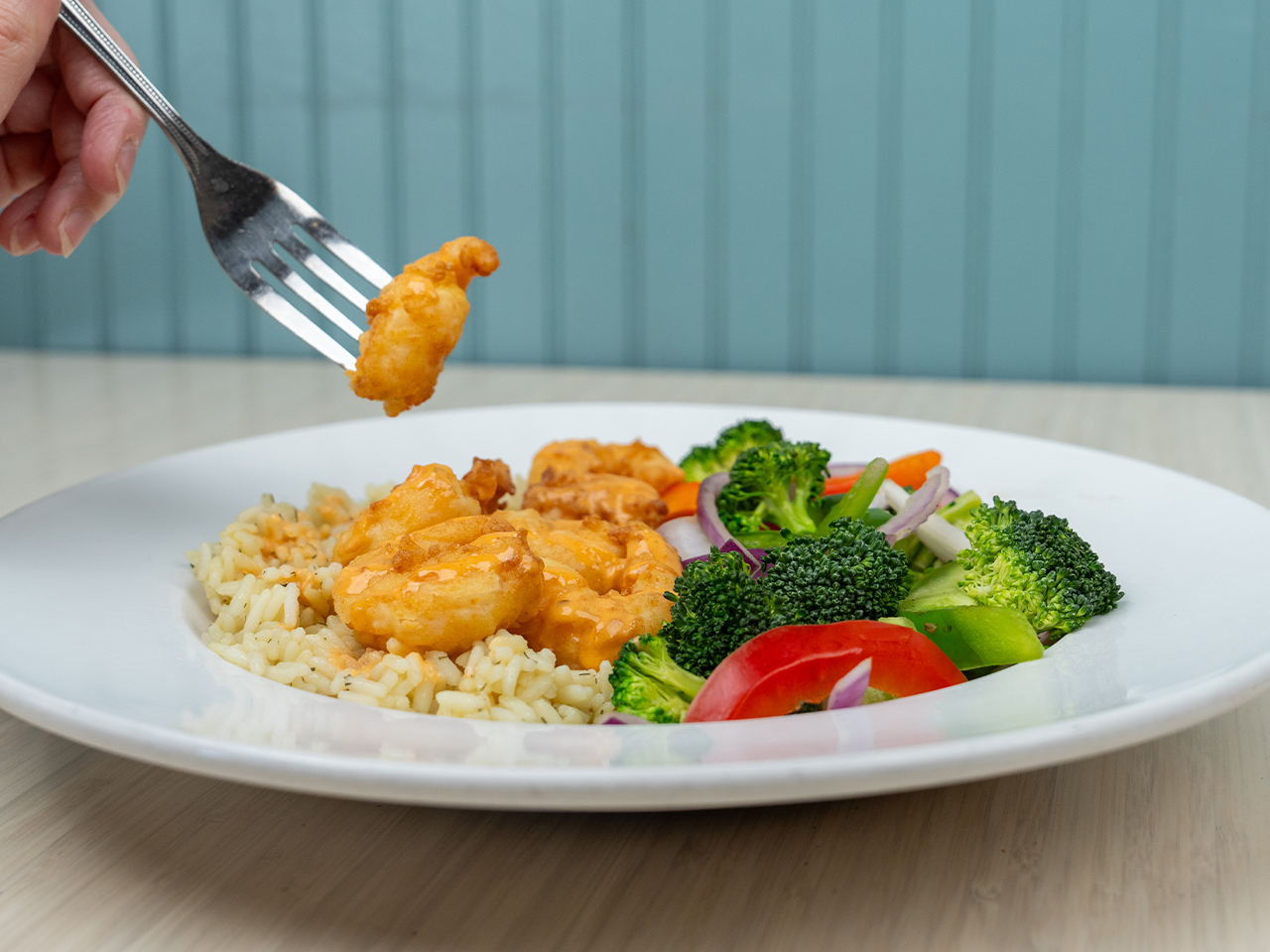 Plate of shrimp, rice, and mixed vegetables with a fork lifting a shrimp.