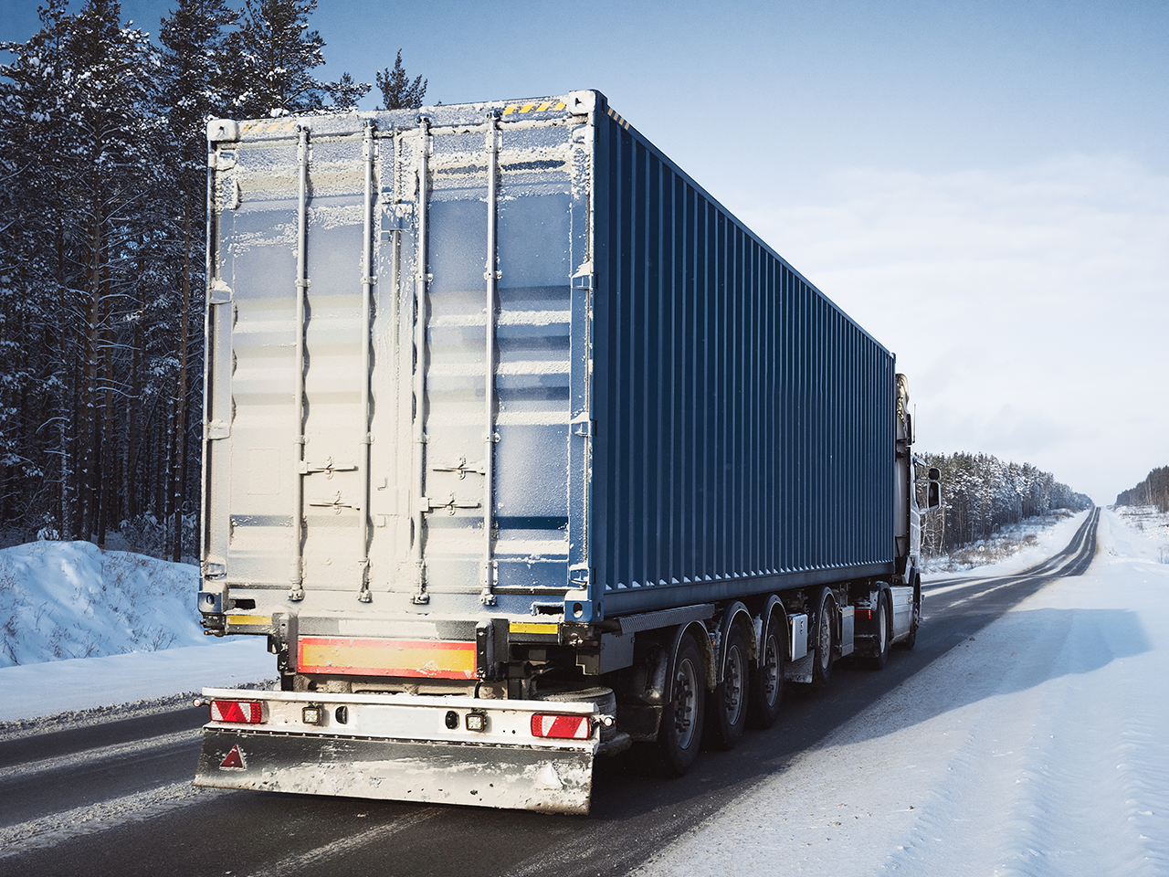 Transport truck carrying a shipping container on a snow-covered highway.