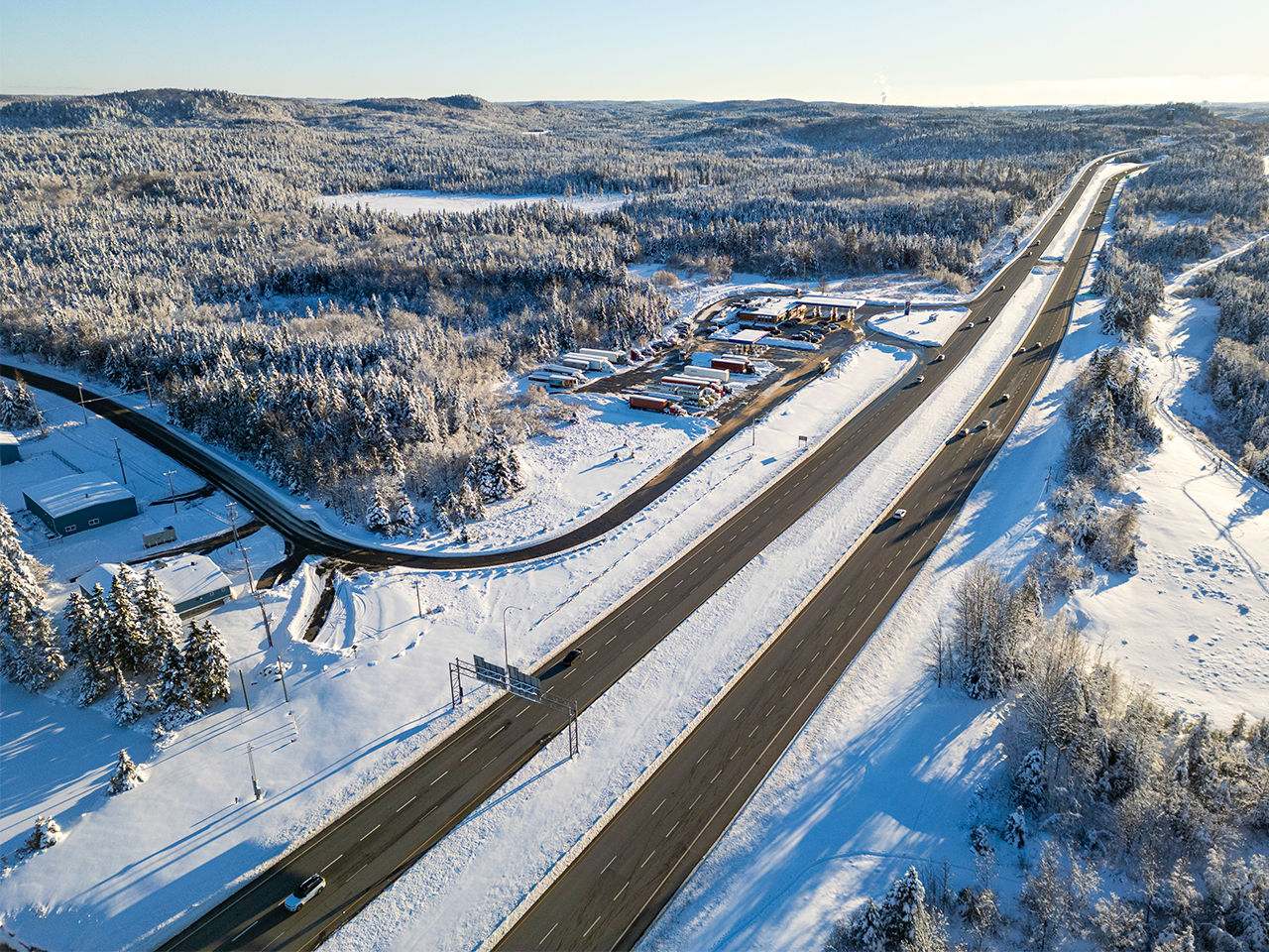 Aerial view of a snow-covered highway running through a winter forest landscape.
