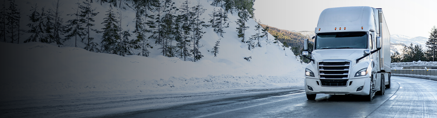 Transport truck driving on a snow-covered highway through a mountain landscape.