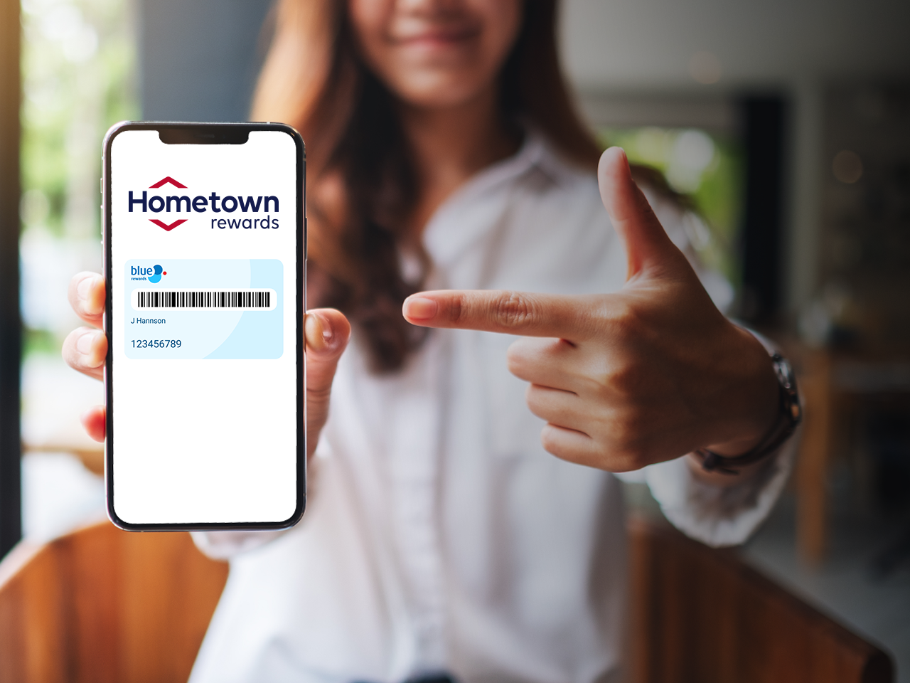 Person holding a smartphone displaying a Hometown Rewards loyalty card and barcode, while pointing at the screen.