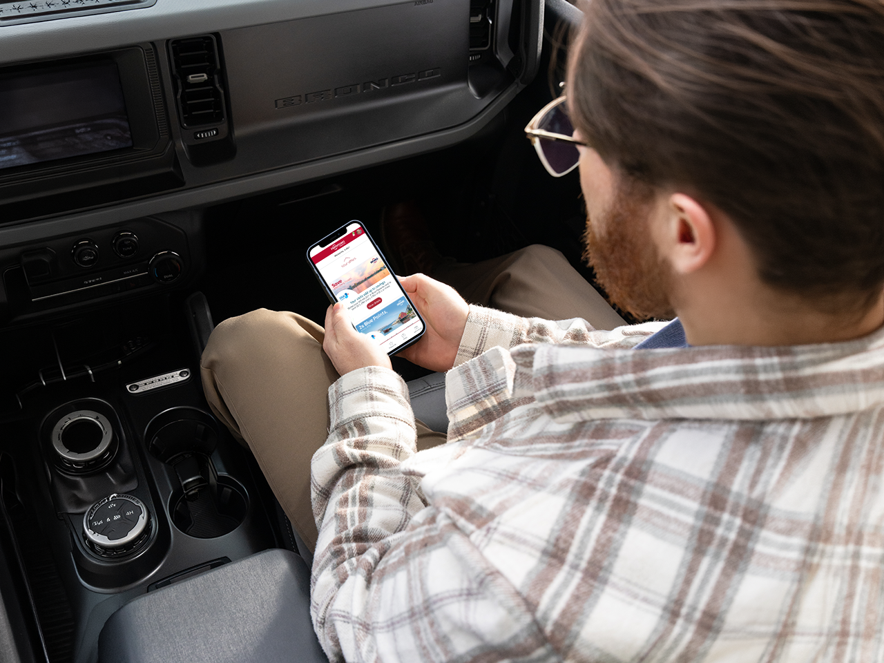 Person seated inside a vehicle using a smartphone to browse the Hometown Rewards app.