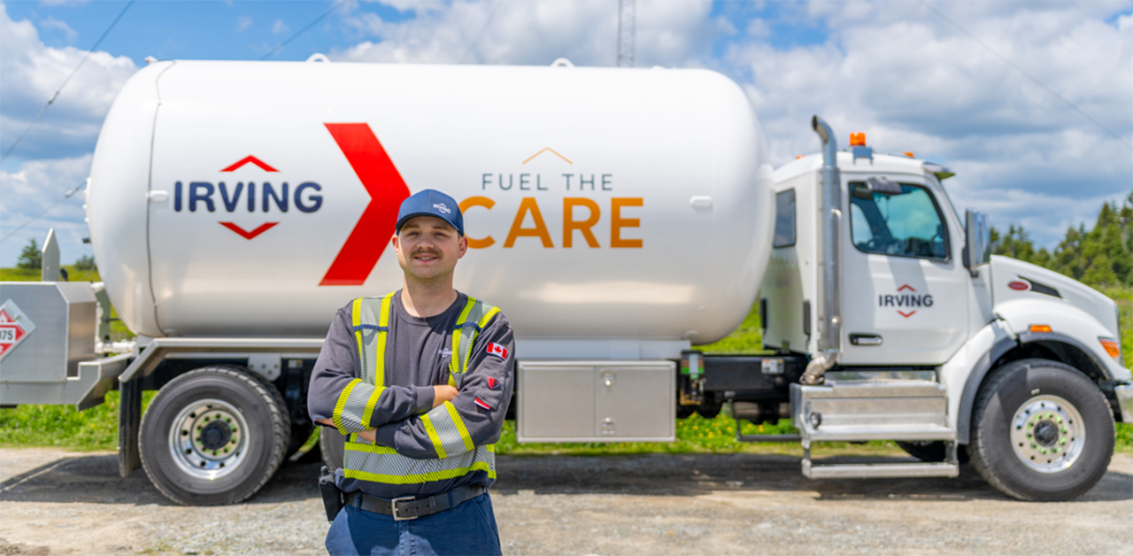 Person wearing a high-visibility work uniform standing with arms crossed in front of an Irving propane delivery truck.