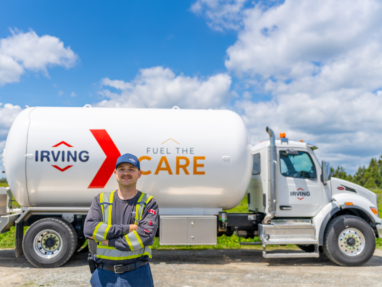 Person wearing a high-visibility work uniform standing with arms crossed in front of an Irving propane delivery truck