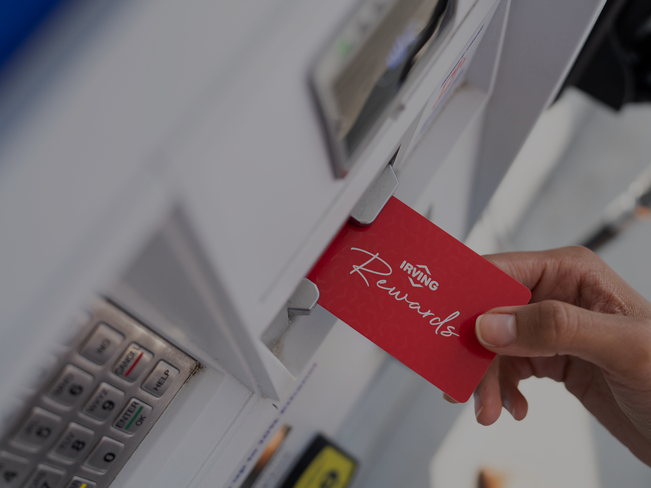 Hand inserting a red Irving Rewards card into a card reader; keypad with Enter, Clear, and Cancel buttons visible nearby.